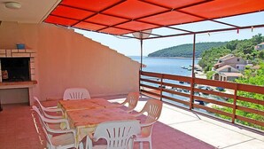 Un espace extérieur abrité, aménagé pour les repas, avec une table et des chaises, offrant une vue sur un plan d’eau et une colline.