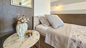 Ein Hotelzimmer mit einem Bett, einem Nachttisch mit Blumenvase, einem Spiegel und einer Wandleuchte.