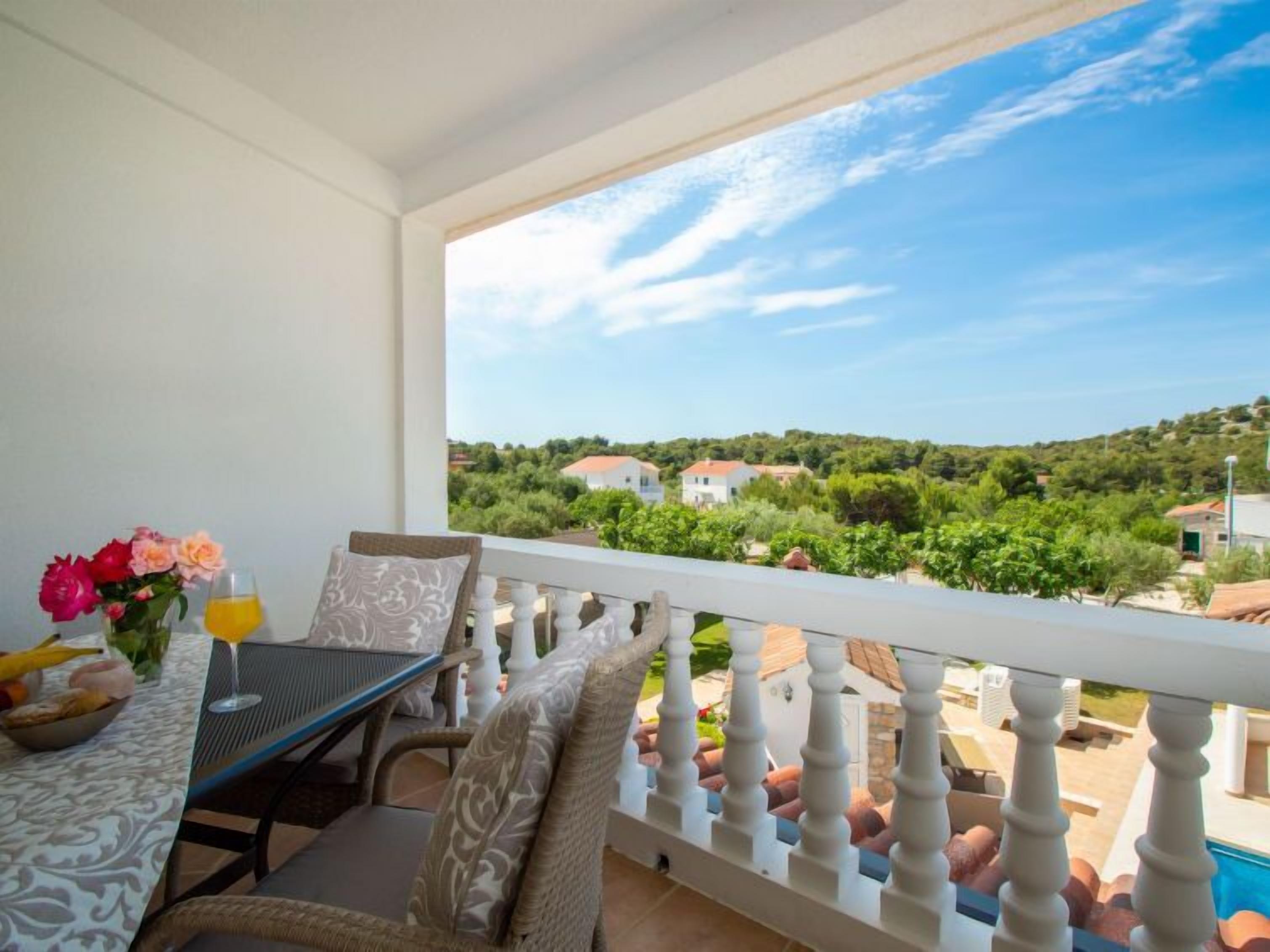 Ein Balkon mit Tisch für zwei Personen, einer Blumenvase und einem Glas Orangensaft.