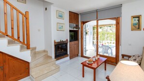 A living room with a fireplace, wooden staircase, and a dining area with a table and chairs.