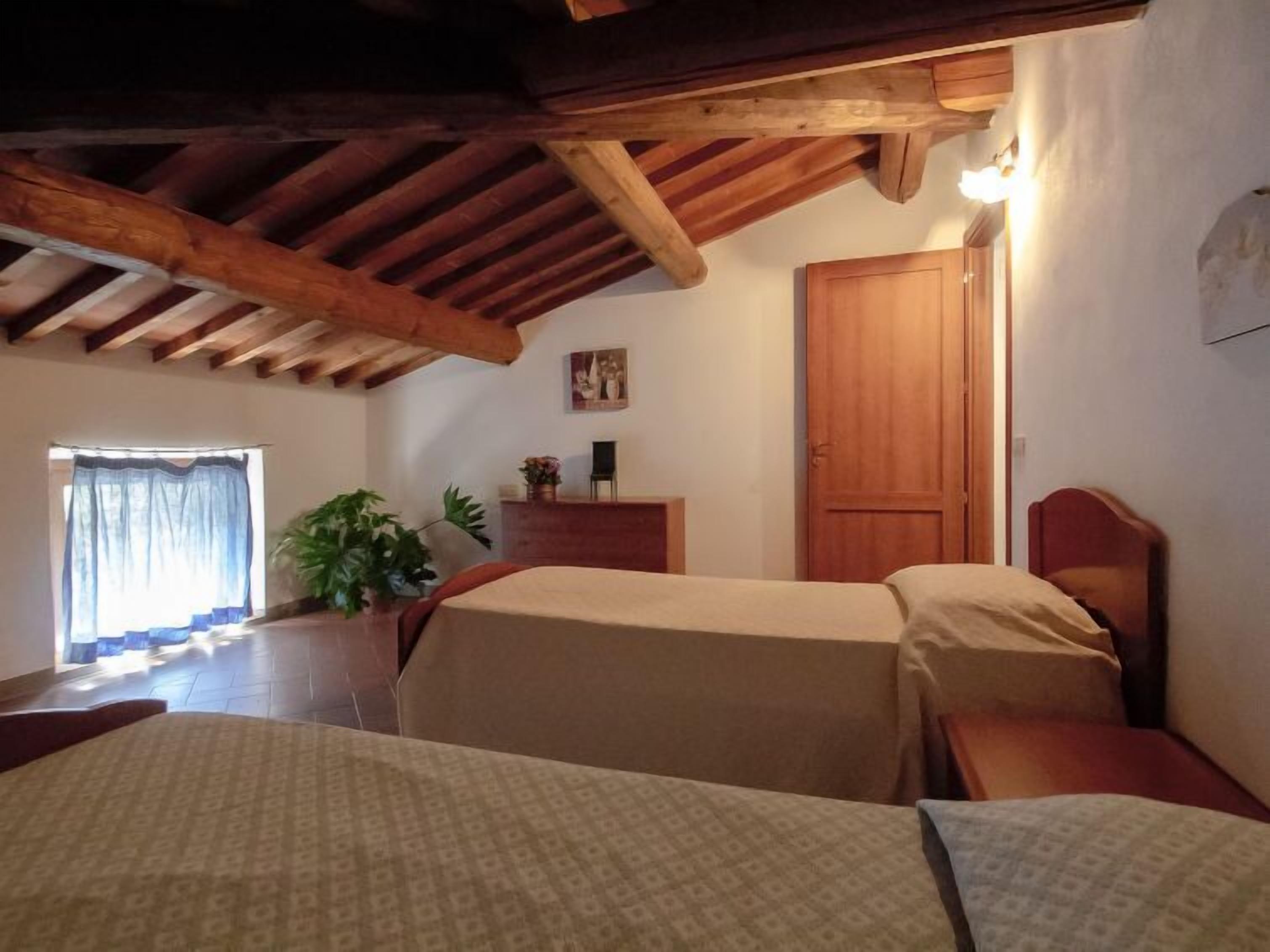 Une chambre avec deux lits, des poutres en bois au plafond, une porte en bois et une fenêtre avec des rideaux.