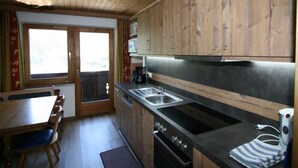 A kitchen with wooden cabinets, a stainless steel sink, a stove, and a dining area with a table and chairs. - Vacation home Hussl by Interhome (Fügen)