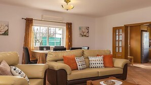 A living room with a sofa, armchairs, a dining table, and a kitchen area. - Das Amendoeiras by Interhome (Alcantarilha)