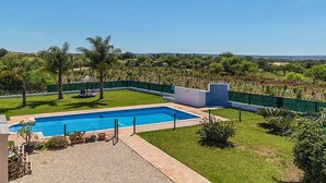 A rectangular swimming pool with a clear blue water, surrounded by a well-maintained lawn and a few palm trees. - Das Amendoeiras by Interhome (Alcantarilha)