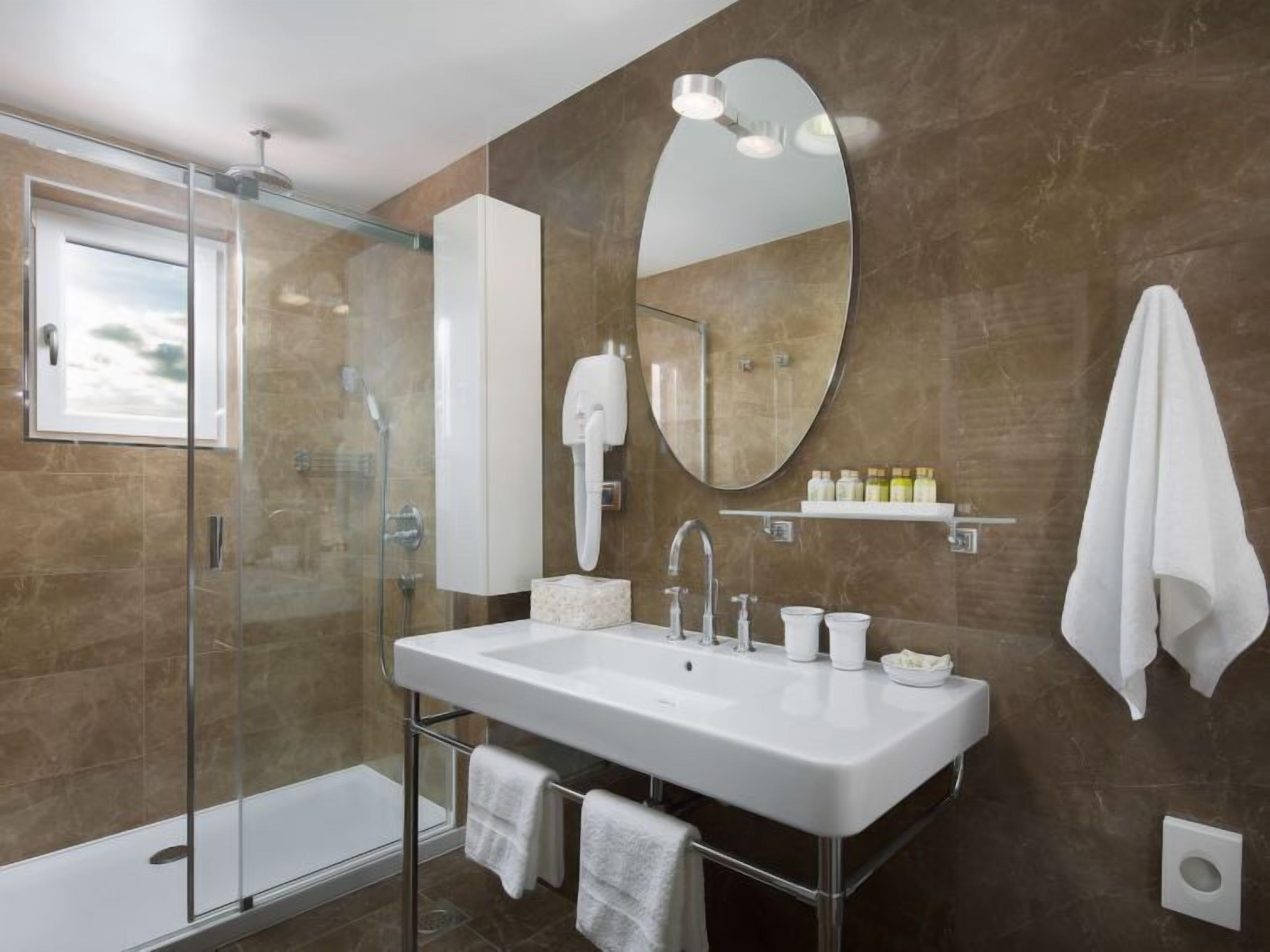 A modern bathroom with a glass-enclosed shower, a large mirror, and a white sink.
