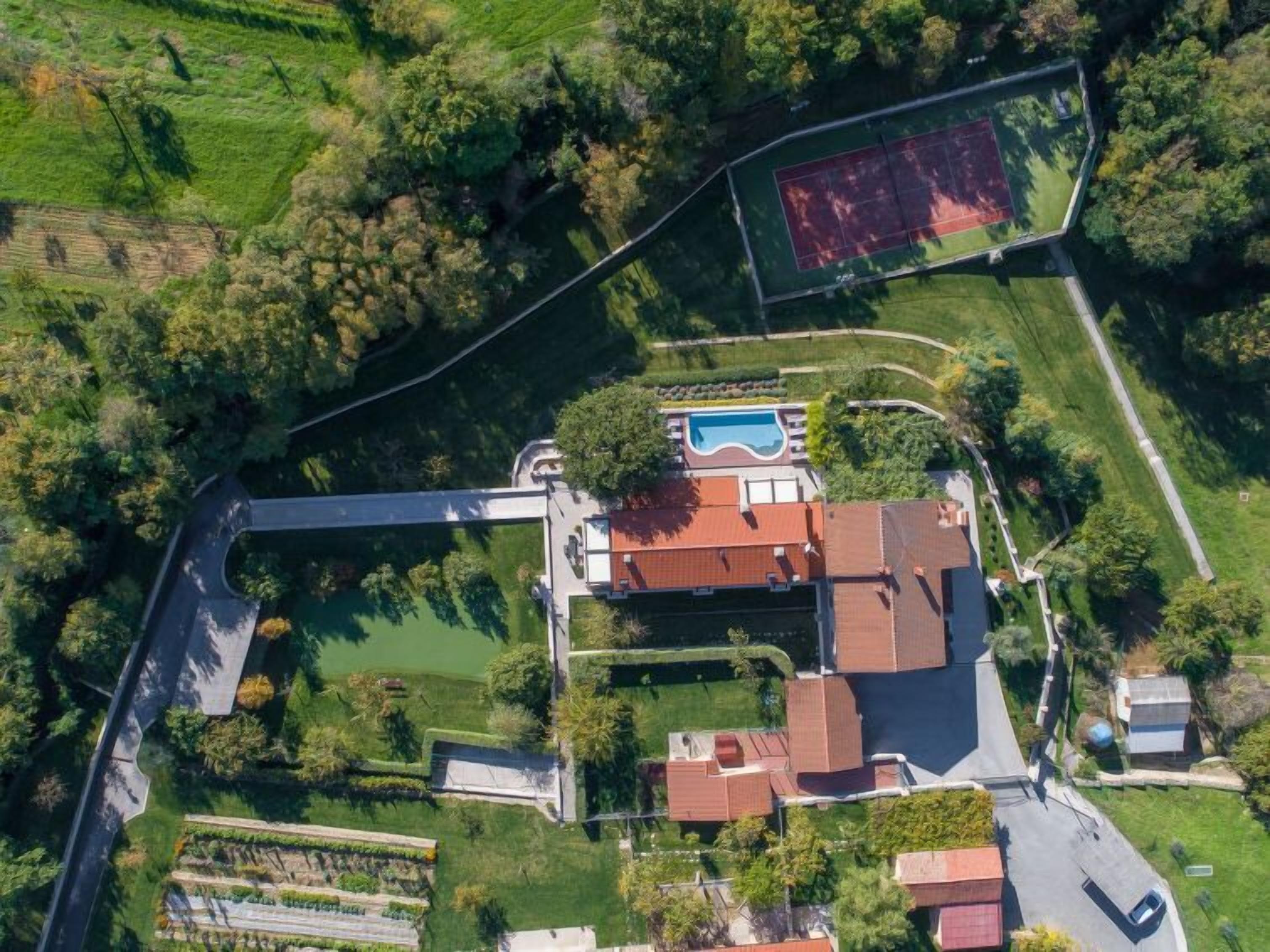 Vista aérea de una propiedad residencial con piscina, cancha de tenis y un amplio jardín.