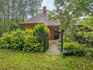 A house with a brick roof, surrounded by dense greenery and a pathway leading to the entrance.