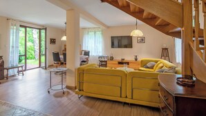 A spacious living area with a wooden staircase, a yellow sofa, a dining table, and a TV mounted on the wall. - Borowikowa by Interhome (Sasino)