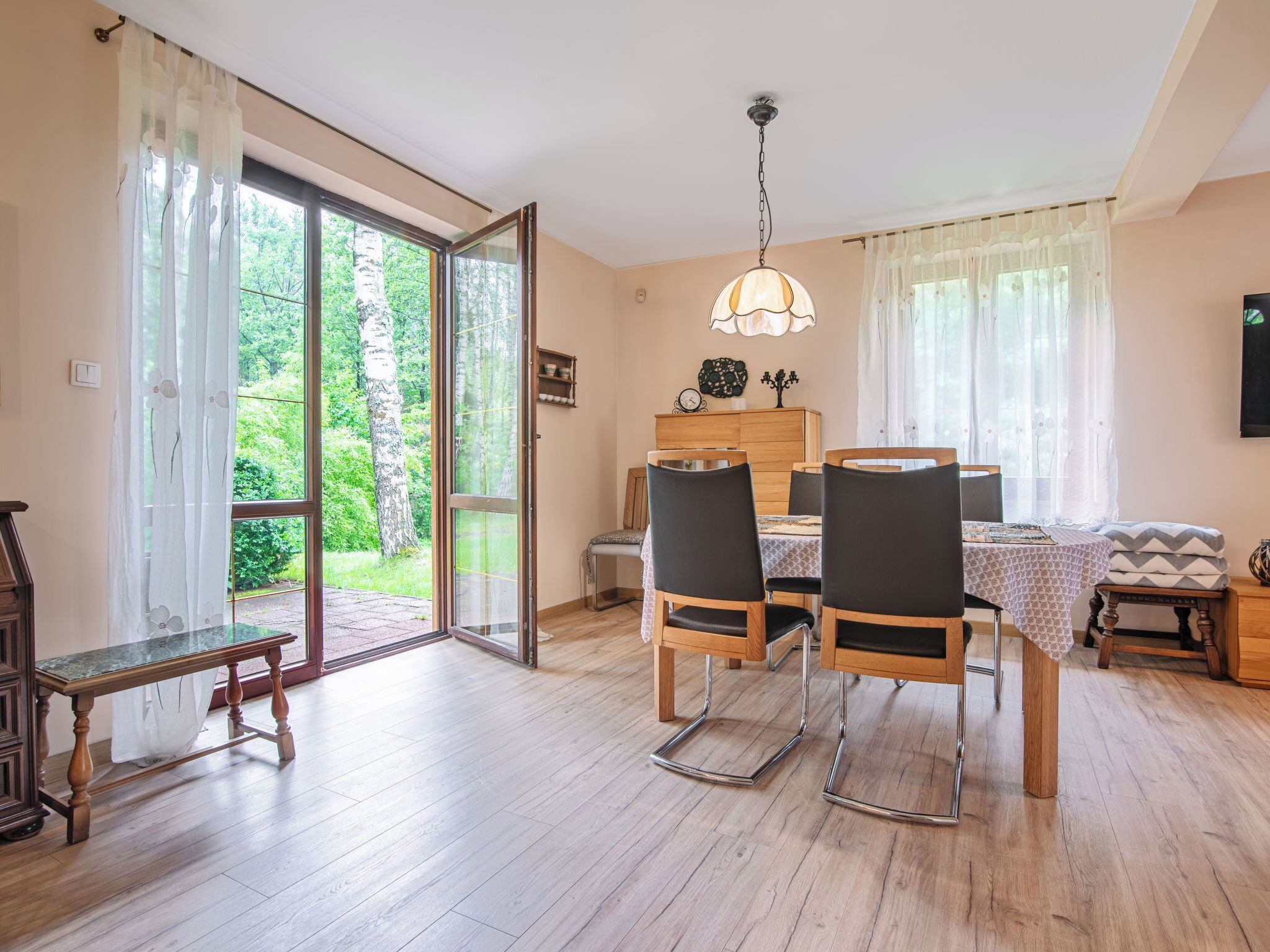 Un espace repas comprenant une table, des chaises et un banc. Une porte-fenêtre coulissante donne accès à un jardin.