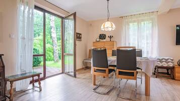 Un espace repas comprenant une table, des chaises et un banc. Une porte-fenêtre coulissante donne accès à un jardin.