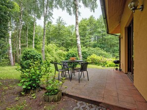 An outdoor patio with a table and chairs, surrounded by lush greenery and tall trees.