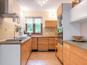 A kitchen with wooden cabinets, a stainless steel sink, and a window with lace curtains.
