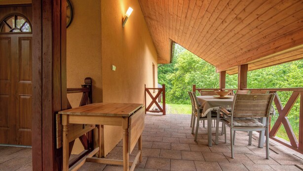 A wooden table and chairs in a covered outdoor area with a view of greenery. - Borowikowa by Interhome (Sasino)
