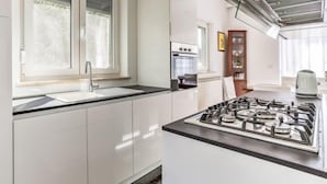 Een moderne keuken met witte kasten, een gasfornuis, een ingebouwde oven en een raam met geëtste glas.