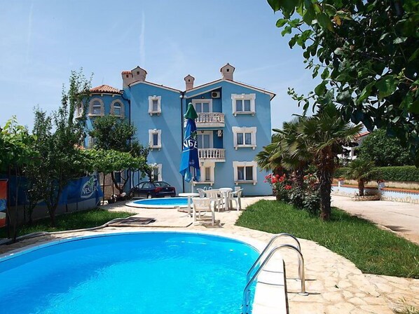 Een hotel met een zwembad, terras en een blauwe gevel.