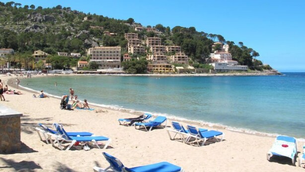 A beach with sun loungers and a rocky hillside in the background.