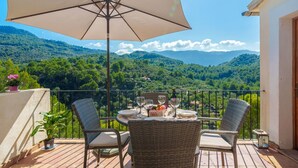 A balcony with wicker chairs, a table set with plates, glasses, and a bottle, and a large umbrella.