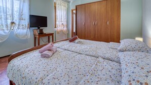 Ein Schlafzimmer mit einem großen Bett, einem Holzschrank, einem Fernseher auf einem Holztisch und einem Fenster mit Vorhängen.