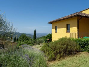 A yellow building with a tiled roof, surrounded by greenery and a view of distant hills. - Cafaggio di Sopra by Interhome (Florence)