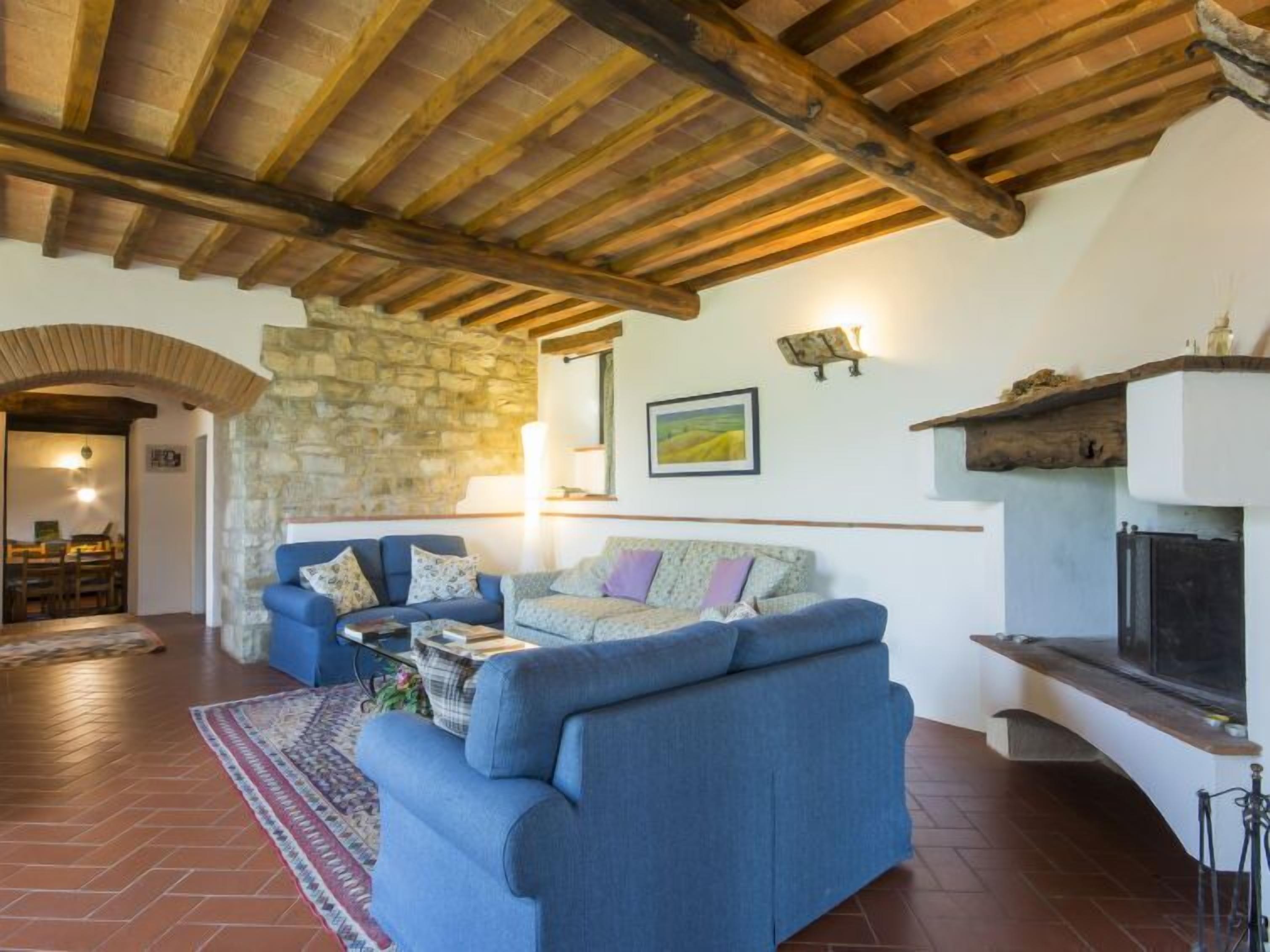 A cozy living room with a stone wall, wooden beams, a blue sofa, and a fireplace.