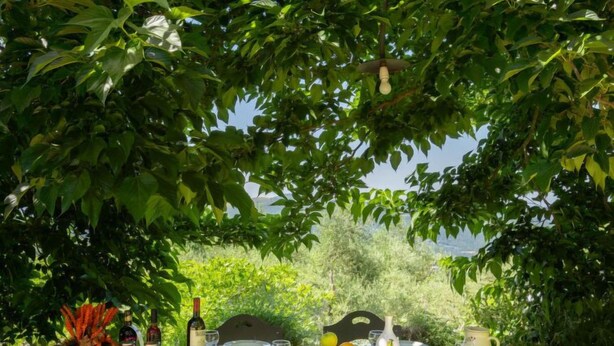 Eettafel buiten gedekt met borden, glazen en een fles wijn, omringd door weelderig groen en een prachtig uitzicht.