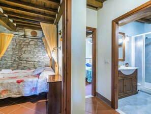 Une chambre à coucher avec un lit, un mur en pierre, un plafond en bois et une salle de bain équipée d’un lavabo et d’un miroir.