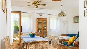 Un coin repas avec des chaises en osier, une table recouverte d’une nappe bleue, un ventilateur de plafond et un luminaire suspendu.