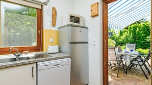 Une cuisine compacte équipée d’un lave-vaisselle, d’un four à micro-ondes et d’un réfrigérateur. Une fenêtre offre une vue sur la verdure, et une porte donne accès à un patio extérieur.