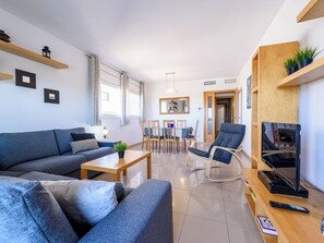 A modern living room with a sofa, coffee table, and TV stand. There is a dining area with chairs and a table.