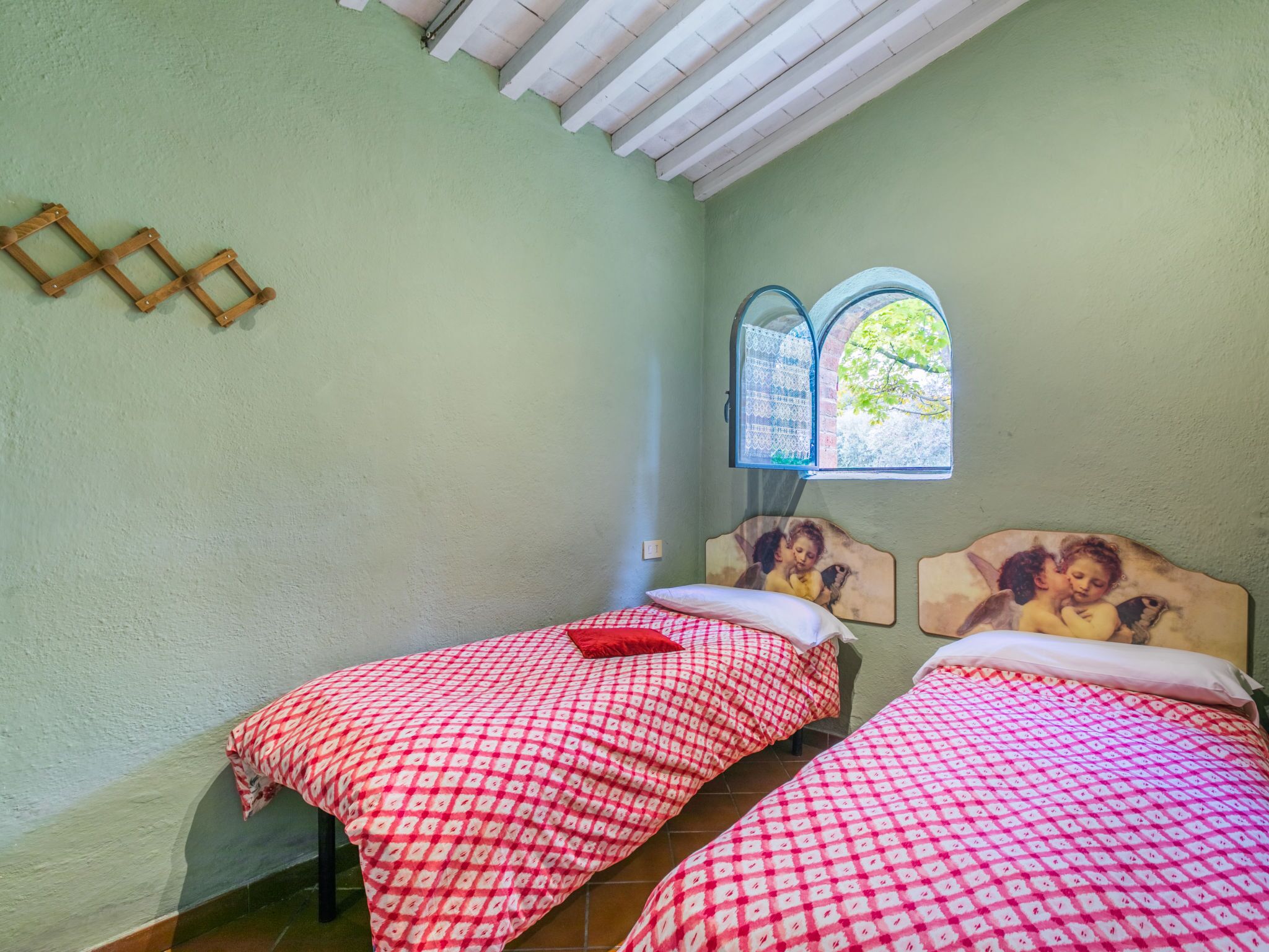Une chambre avec deux lits, une fenêtre donnant sur un paysage verdoyant et un treillis en bois sur le mur.