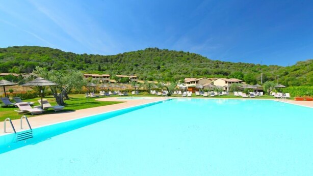 A resort with a large swimming pool, sun loungers, and villas in a hilly landscape.