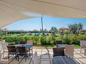 Un espace extérieur aménagé en terrasse, avec des meubles en osier, une piscine et des parasols pour créer de l’ombre.