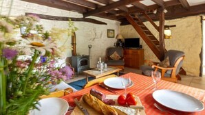A cozy living room with a fireplace, wooden beams, a dining table set with food, and a staircase.