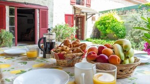 A breakfast table with plates, a coffee pot, a basket of bread, a basket of fruit, and a glass of orange juice.