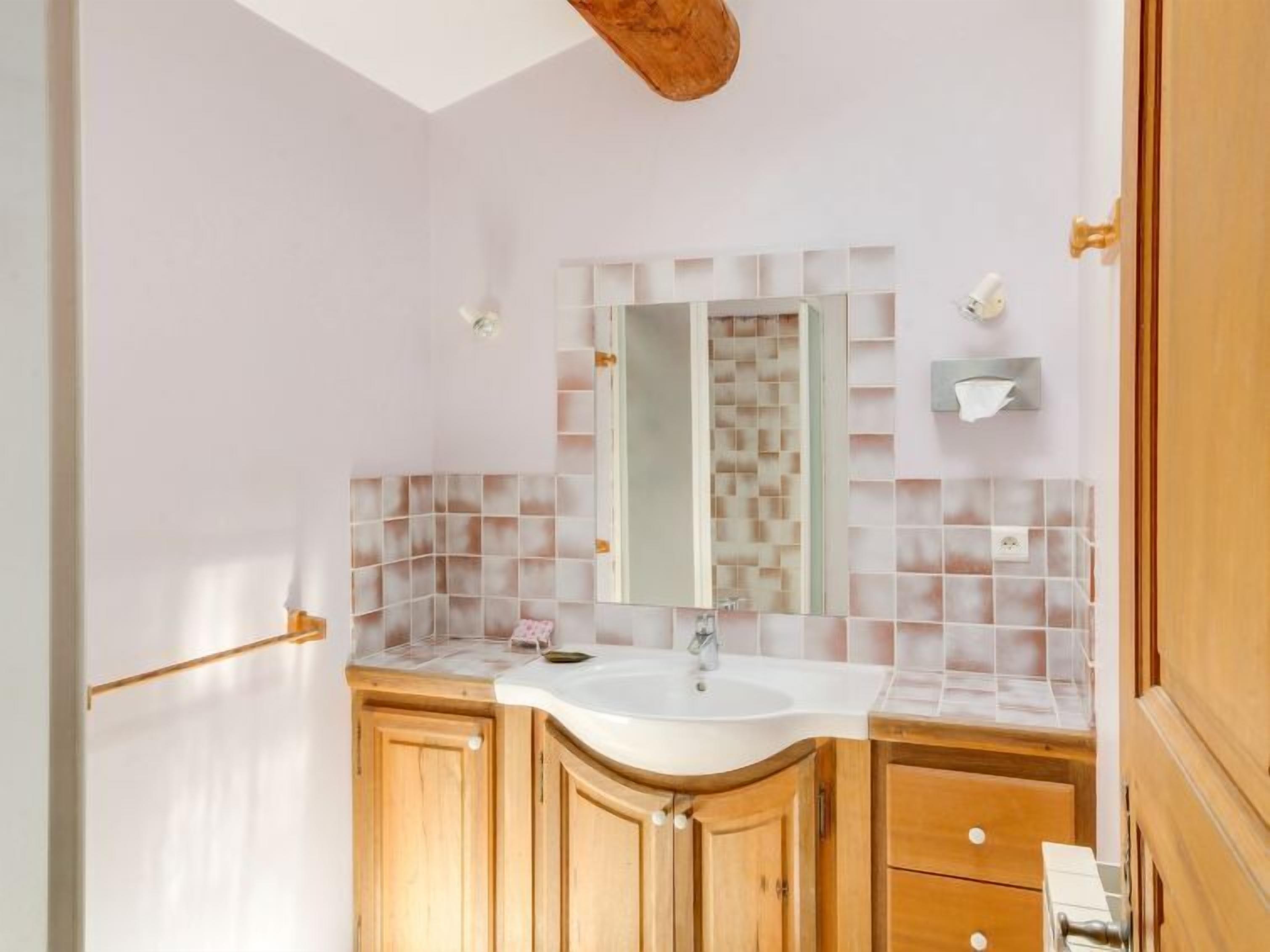 Une salle de bain avec un lavabo blanc, des meubles en bois, un miroir et un mur recouvert de carreaux.