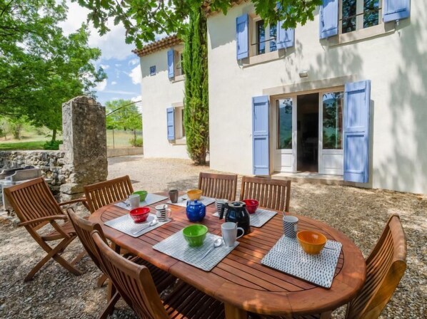 An outdoor dining area with a round wooden table, surrounded by chairs, set on a gravel surface.