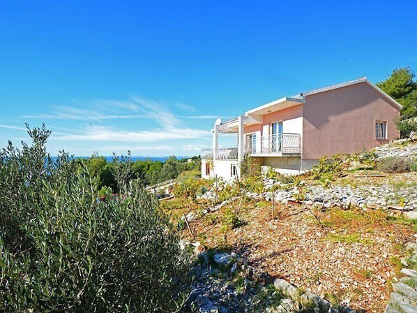 A two-story house with a balcony, surrounded by olive trees and a rocky landscape. - Vacation home Mira by Interhome (Primošten)