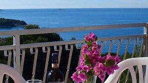 Un balcón con una mesa, una botella de vino y un florero, con vistas a la costa.