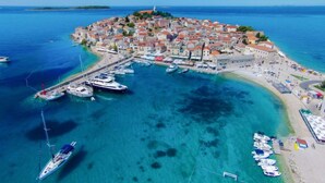 Vista aérea de un pueblo costero con un puerto deportivo, aguas azules cristalinas y una iglesia destacada en una colina.