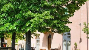 A courtyard with a large tree, a building with arched windows, and potted plants. - Chiantishire retreat by Interhome (Barberino Valdelsa)