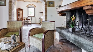 A cozy living room with wicker furniture, a fireplace, and a stone archway leading to a dining area. - Chiantishire retreat by Interhome (Barberino Valdelsa)
