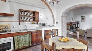 A kitchen with an island, wooden cabinets, a microwave, and a dining area with a table set for two. - Chiantishire retreat by Interhome (Barberino Valdelsa)