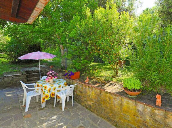 Una terrazza esterna con tavolo e sedie, circondata da vegetazione e un muro in pietra.