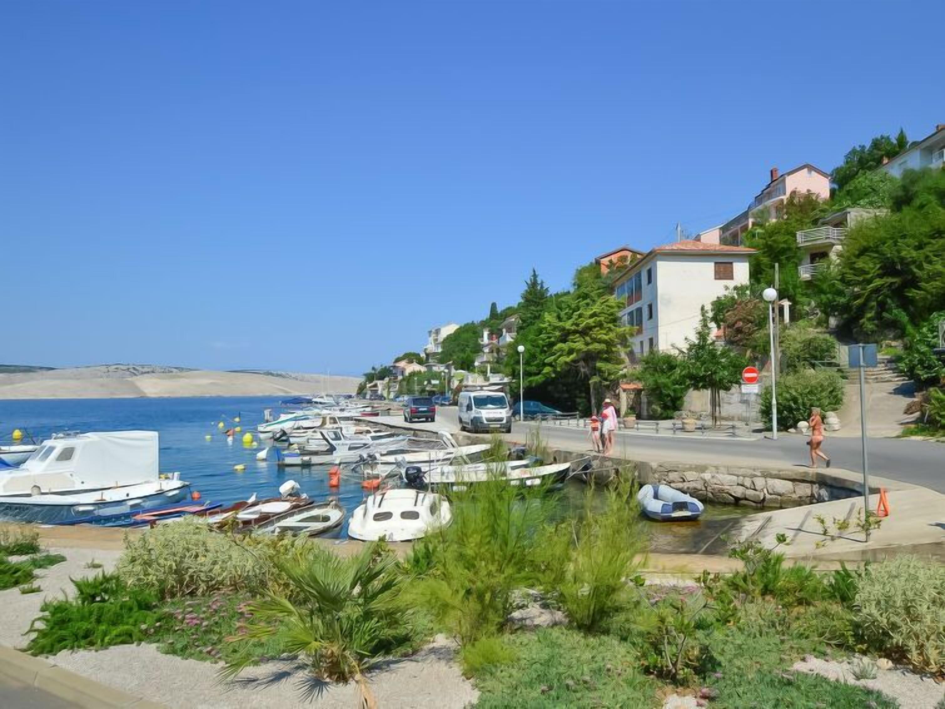 A coastal marina with boats docked, a sandy beach, and residential buildings with balconies overlooking the water.