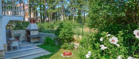 A stone barbecue area with a stone fireplace, surrounded by a well-maintained lawn and flowering plants.