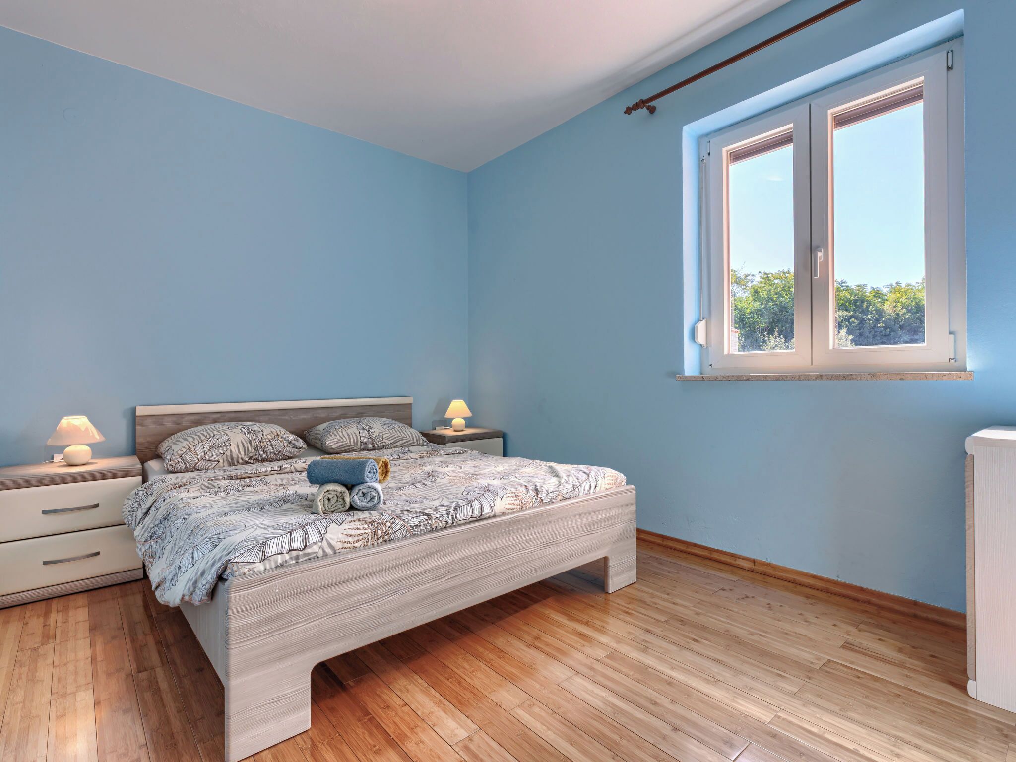 Une chambre à coucher avec un lit, deux tables de chevet avec des lampes, une fenêtre et un radiateur.