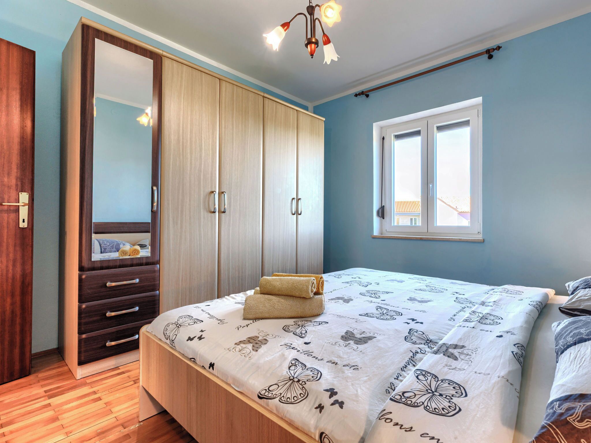 A bedroom with a bed, a wardrobe, a mirror, and a window.
