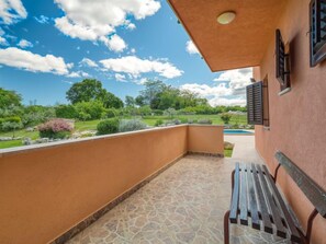 Un balcón con suelo de piedra, una banca y vistas a un jardín y una piscina.
