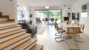 Een modern interieur met een trap, een eetgedeelte met rieten stoelen en een televisie.