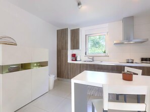 A modern kitchen with white cabinetry, a window, and a white dining table.